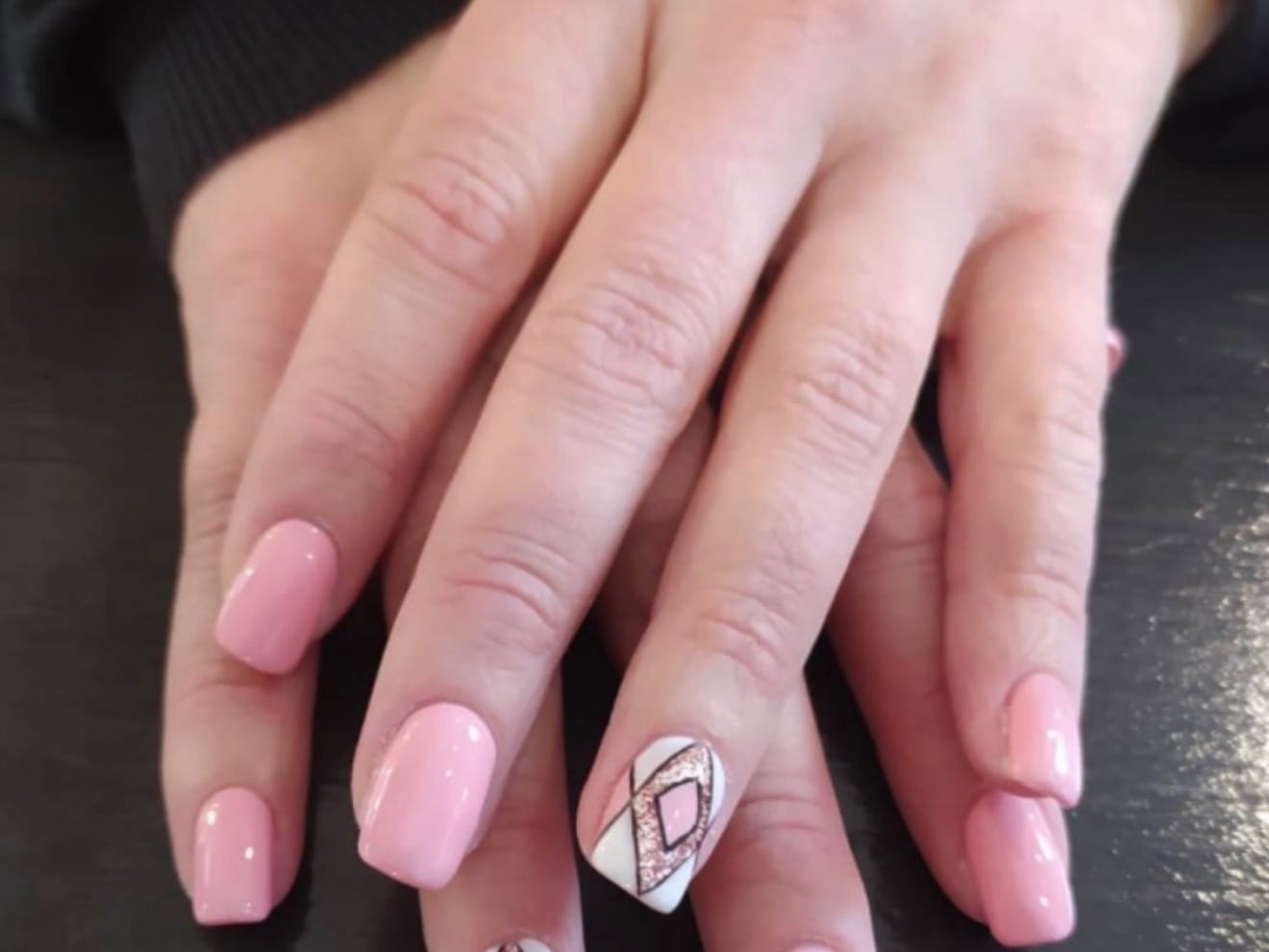 Unghie con smalto rosa e un decoro geometrico bianco e rame sull'anulare.