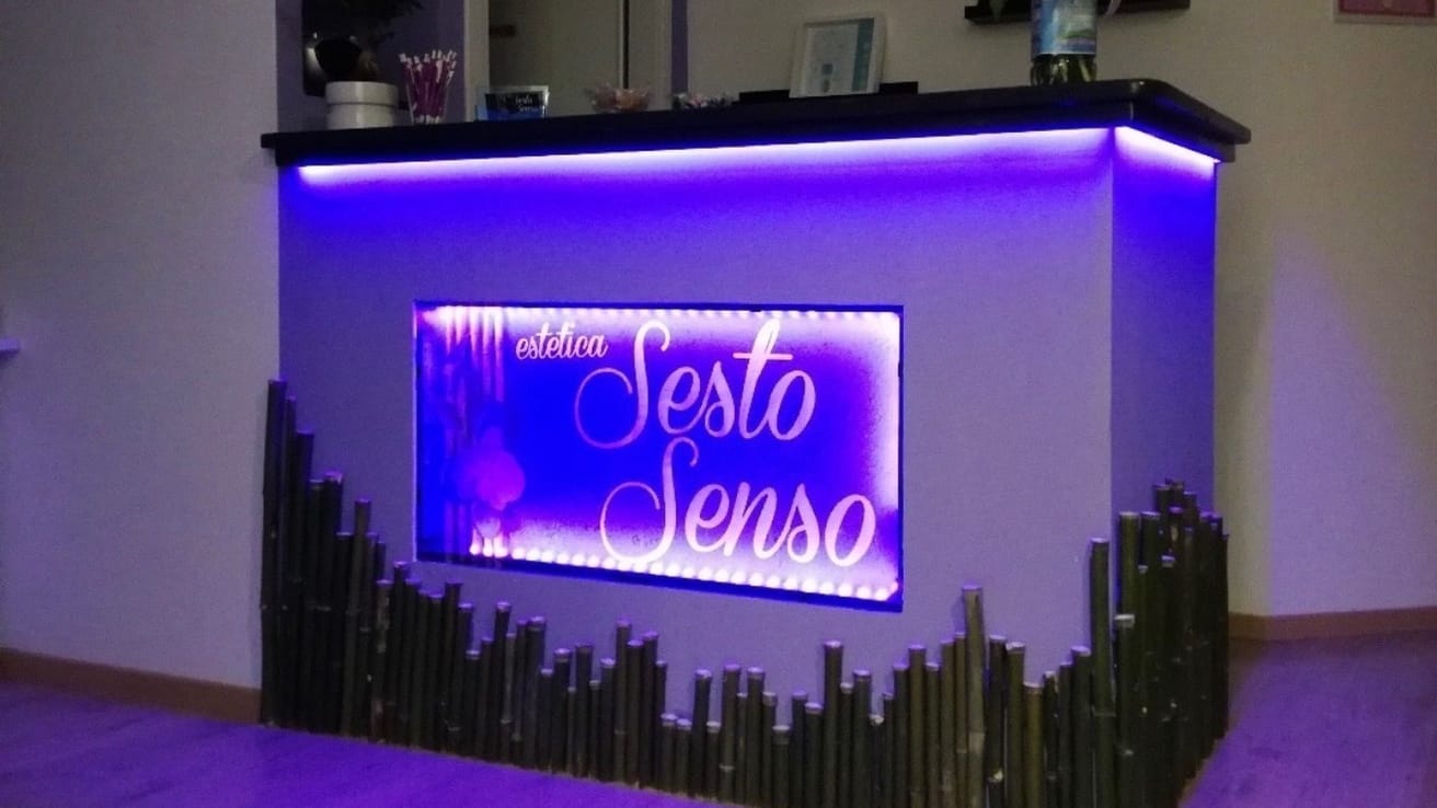 Il banco dell'accoglienza di Estetica Sesto Senso: l'insegna luminosa del centro e la fascia di bambù sotto il piano.
